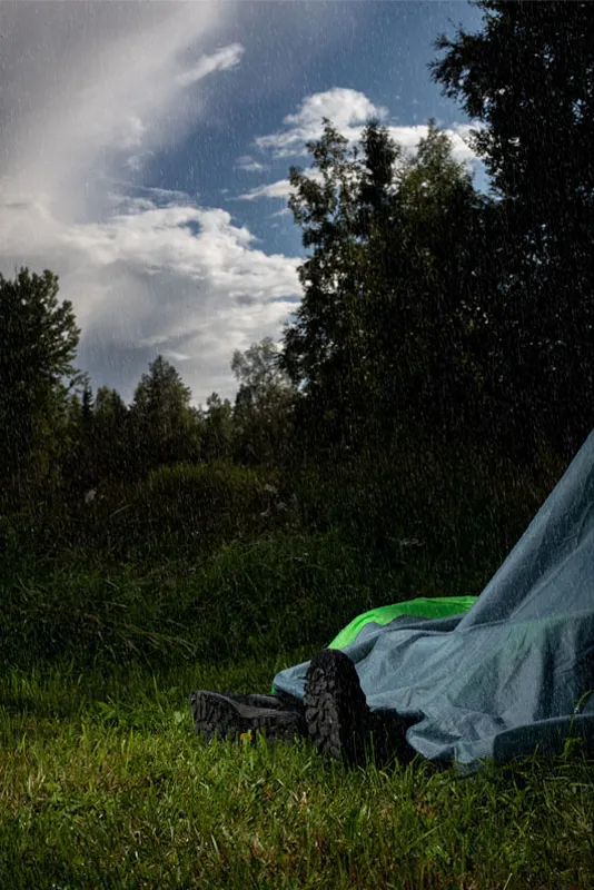 kuva romahtaneesta teltasta josta näkyy miehen jalat. Teltan päälle sataa vettä.